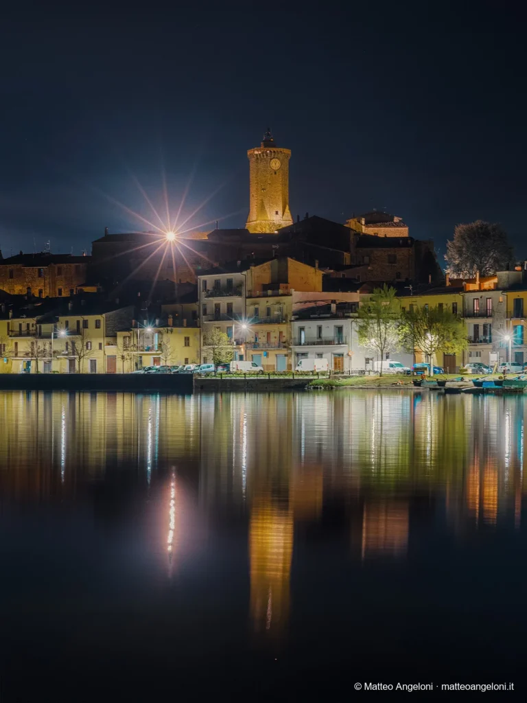 Marta illuminata di notte con riflessi sul Lago di Bolsena