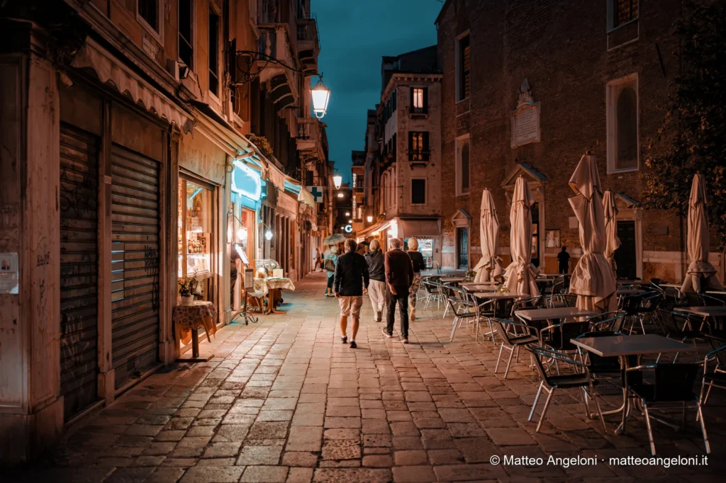 Ristoranti e passanti lungo una calle veneziana di sera
