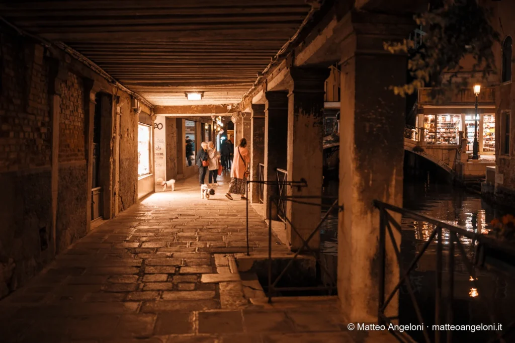 Passanti sotto un portico veneziano illuminato di notte